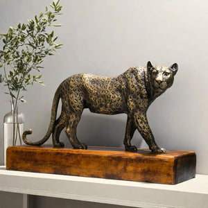 Antique bronze leopard statue displayed indoors alongside greenery plant decor on wood base