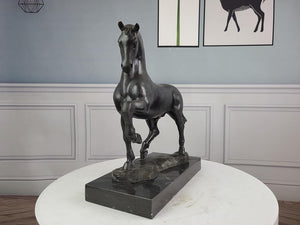 Second view of black bronze striding stallion statue displayed against blue gray wall interior