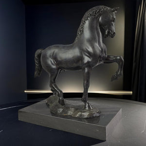 Black bronze striding stallion statue front view displayed against dark moody interior background