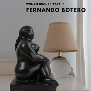 Botero bronze seated woman figurine displayed beside lamp in bedroom setting
