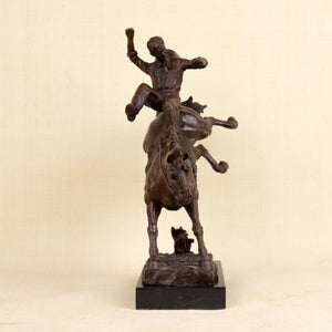 Side view of Bronco Buster bronze bucking combat sculpture showing cowboy raising arm above rearing horse