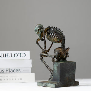 Bronze skeleton Thinker statue displayed on wooden table in modern interior room setting