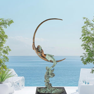 Bronze mermaid on crescent moon sculpture Moonlight Siren full view ocean backdrop