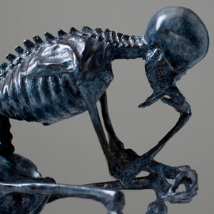 Bronze skeleton Thinker statue in blue-grey patina on bookshelf showing front detail and base