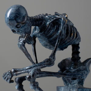 Close-up back view of bronze skeleton Thinker statue in blue-grey patina showing ribcage detail
