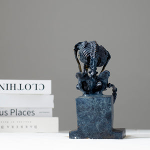 Close-up top view of bronze skeleton Thinker statue in blue-grey patina showing detailed skull and spine
