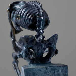 Close-up back view of bronze skeleton Thinker statue in blue-grey patina showing ribcage detail