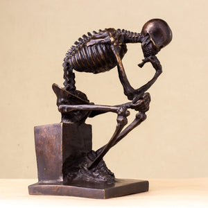 Bronze skeleton Thinker statue in brown bronze finish three-quarter angle view on beige background