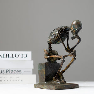 Bronze skeleton Thinker statue displayed on wooden table in modern interior room setting