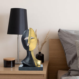 Cubist mask bronze sculpture displayed alongside table lamp in modern bedroom interior setting