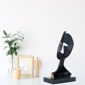 Pair of cubist mask bronze sculptures displayed together with indoor plant in lifestyle setting