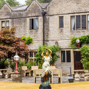 Demeter goddess bronze statue displayed in European estate garden beside stone architecture as outdoor sculpture