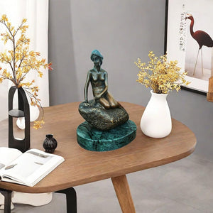 Little mermaid bronze sculpture on coffee table beside books flowers interior display