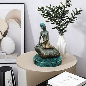 Little mermaid bronze sculpture displayed in living room beside vase and plants