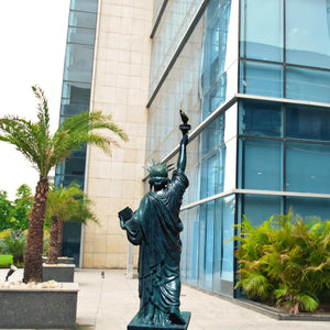 Verdigris blue bronze Statue of Liberty displayed outdoors near modern building with palm trees