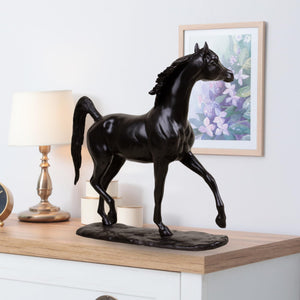 Midnight black Arabian stallion bronze sculpture displayed on table beside lamp and framed art