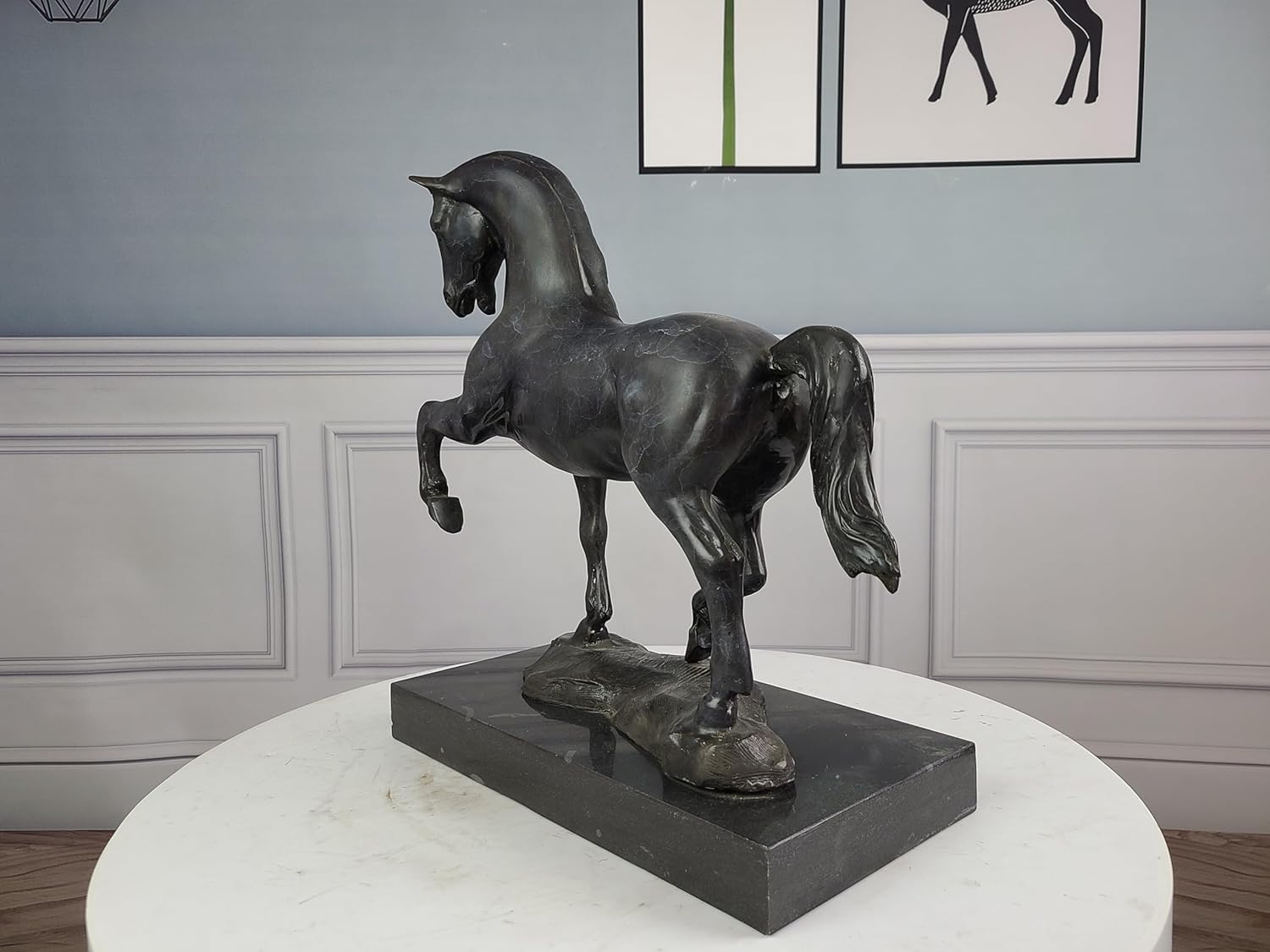 Black bronze striding stallion statue displayed against blue gray wall with framed art decor
