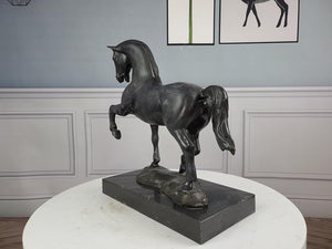 Black bronze striding stallion statue displayed against blue gray wall with framed art decor