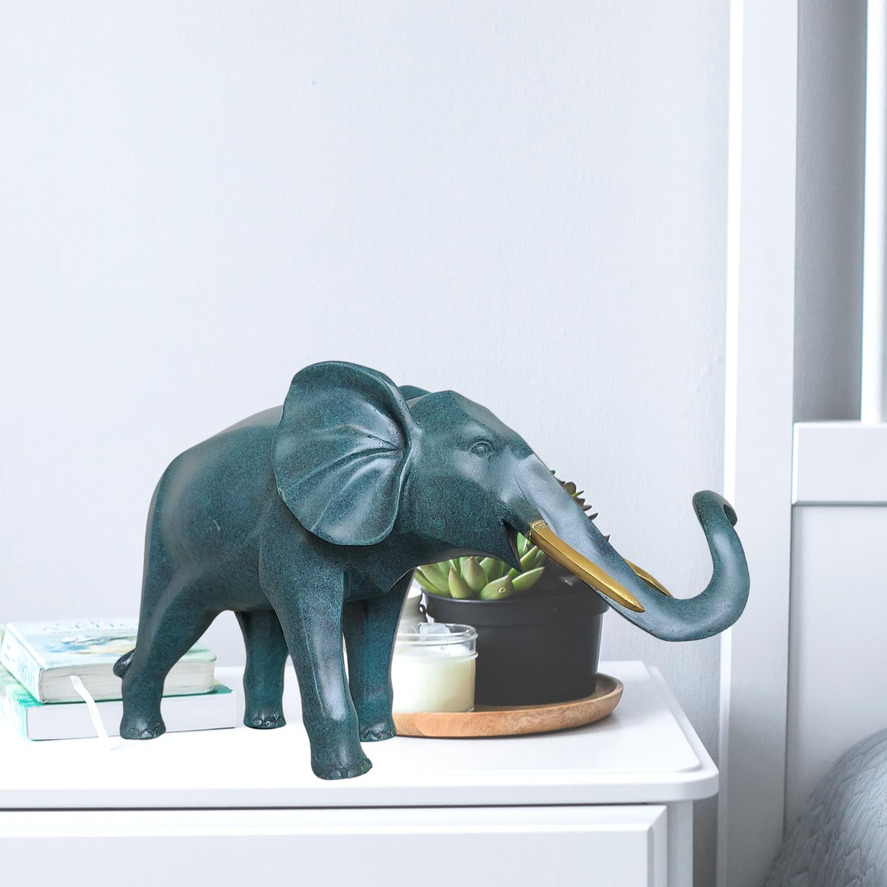 Blue bronze elephant statue on bookshelf beside books and desk accessories as office decor accent