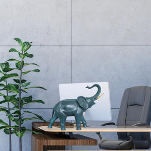 Blue bronze elephant statue with trunk down beside indoor plant against gray wall background