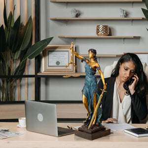 Bronze Lady Justice Themis statue on female lawyer desk with attorney on phone in law office