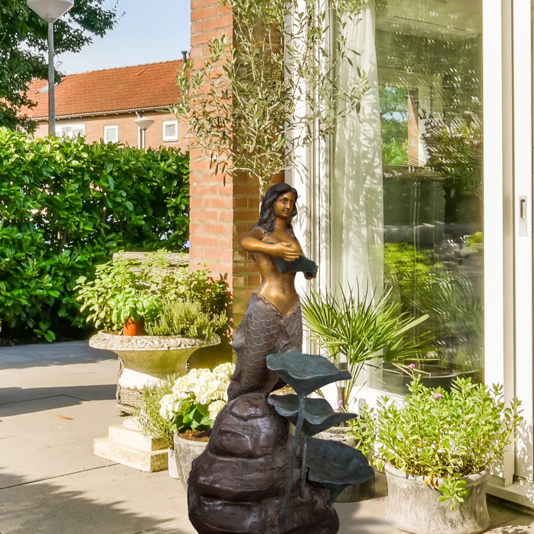 Bronze mermaid garden sculpture displayed along garden pathway lush greenery