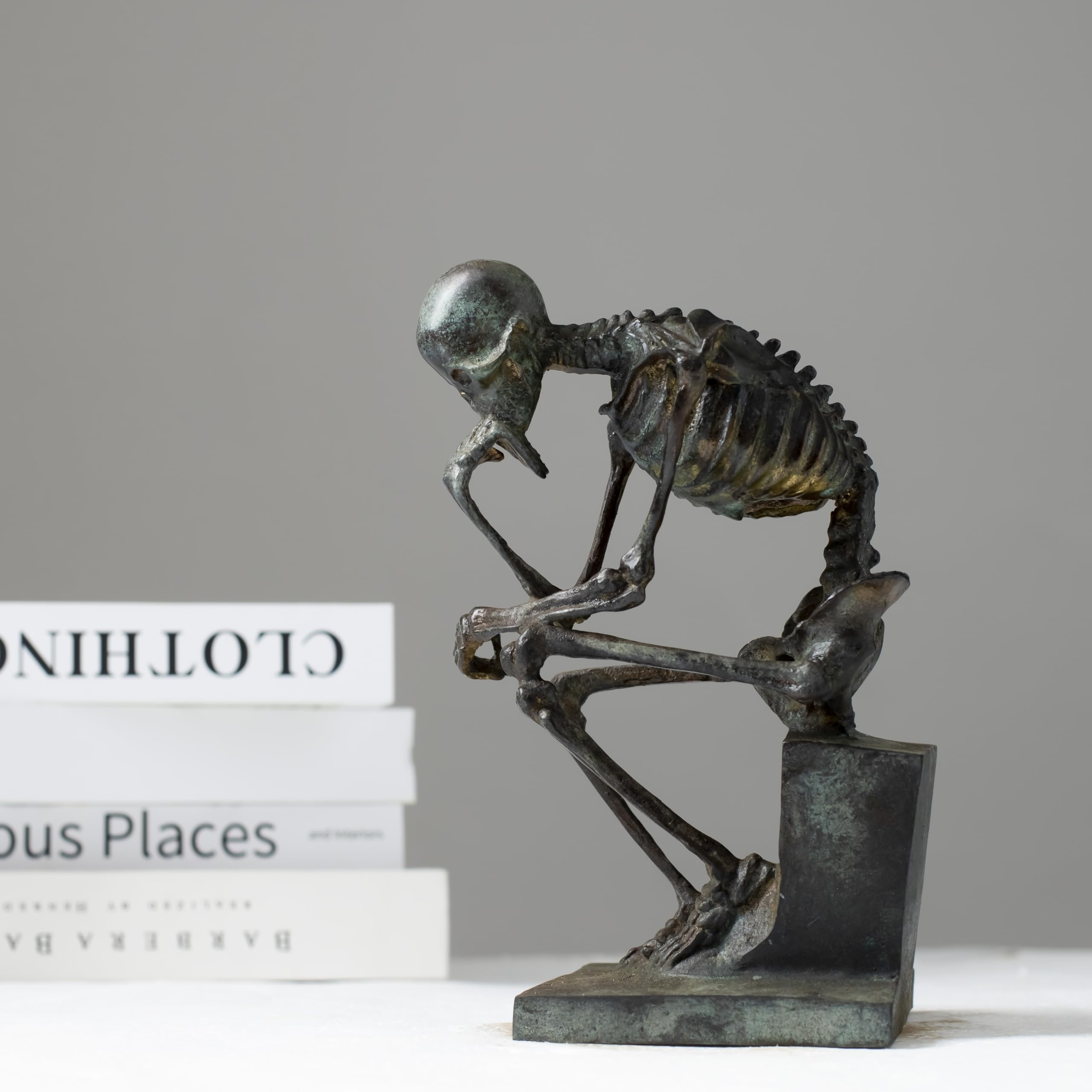 Bronze skeleton Thinker statue in antique grey bronze finish displayed on bookshelf beside books