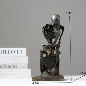 Bronze skeleton Thinker statue in antique grey finish beside decorative glass vase