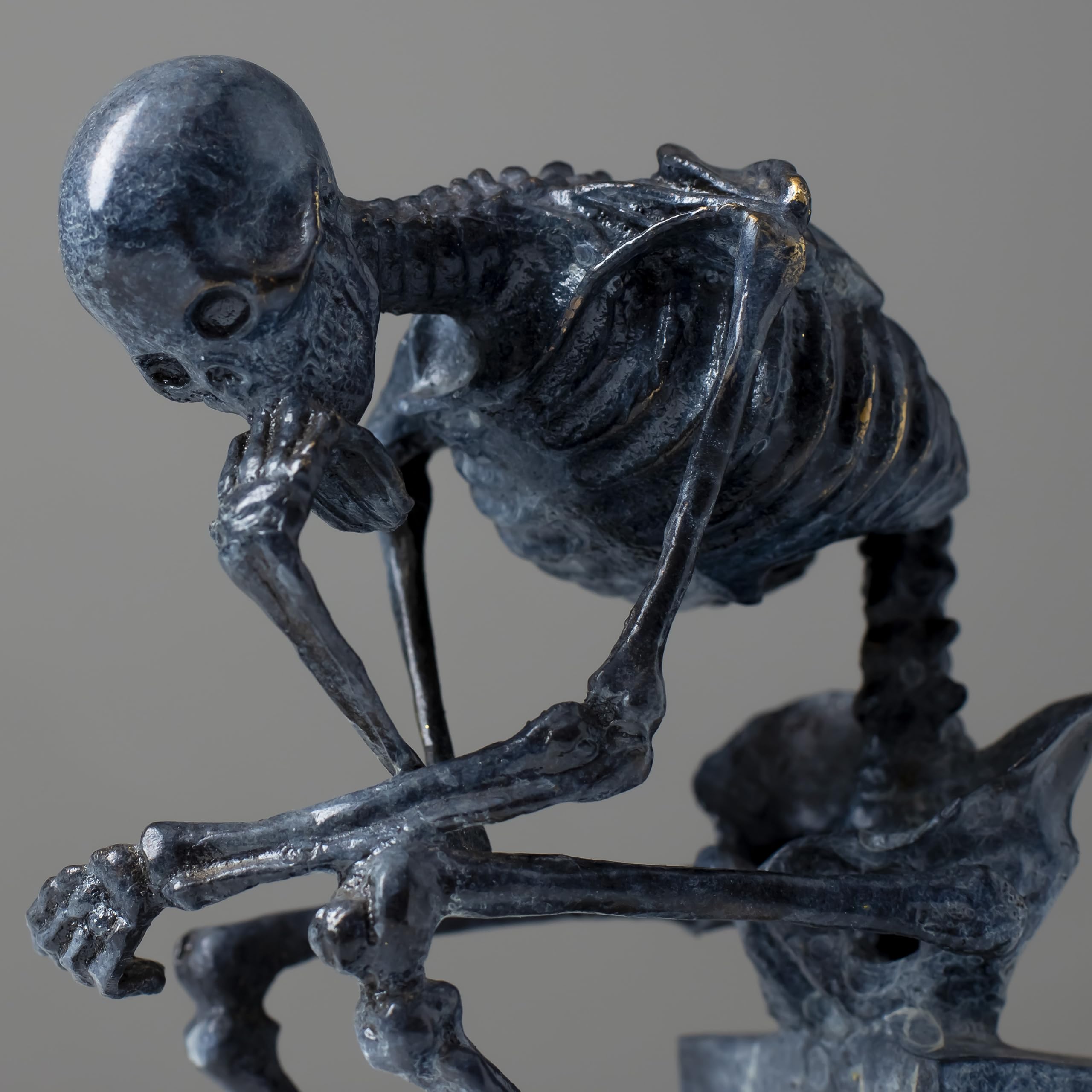Close-up back view of bronze skeleton Thinker statue in blue-grey patina showing ribcage detail