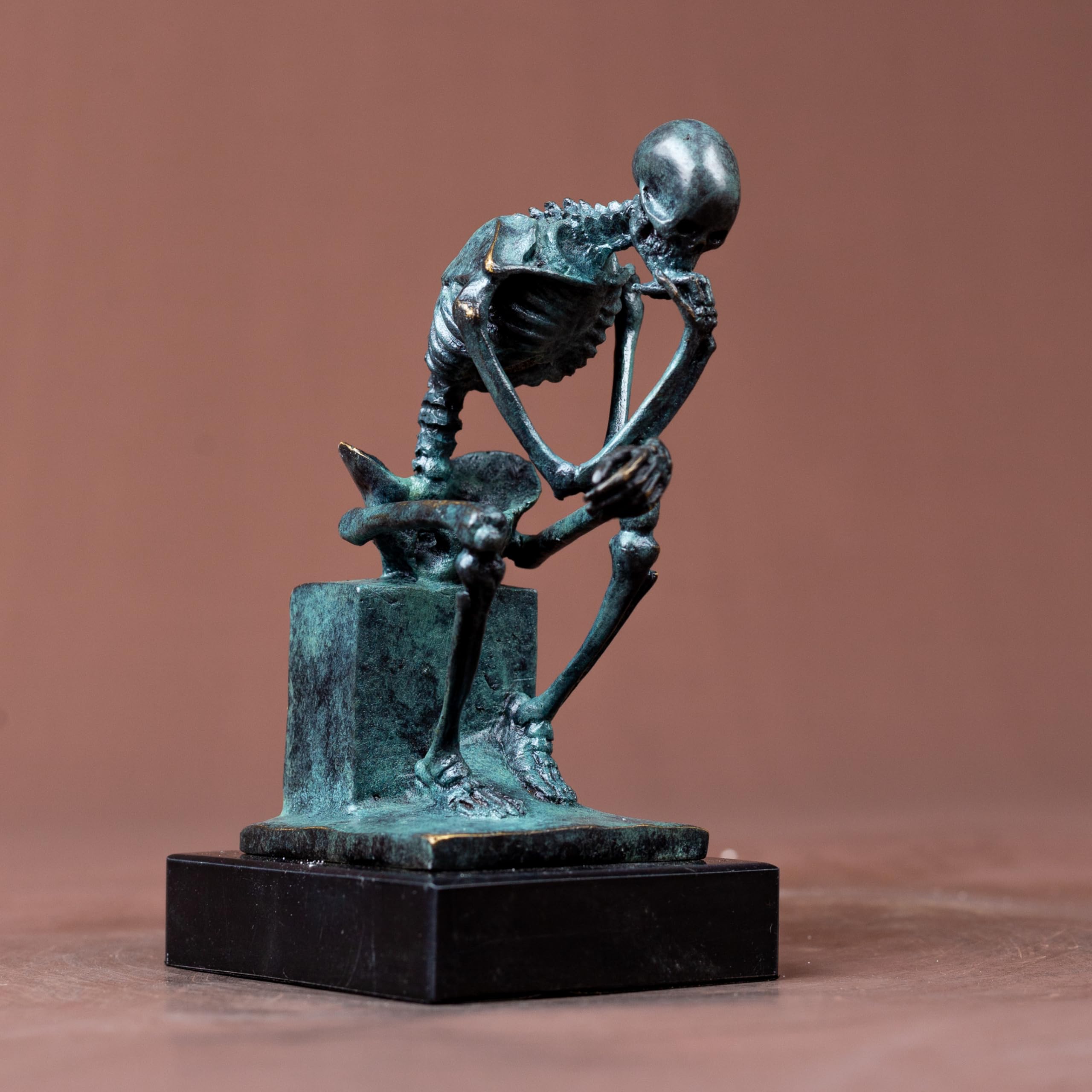 Bronze skeleton Thinker statue in blue-grey finish side view on warm brown background