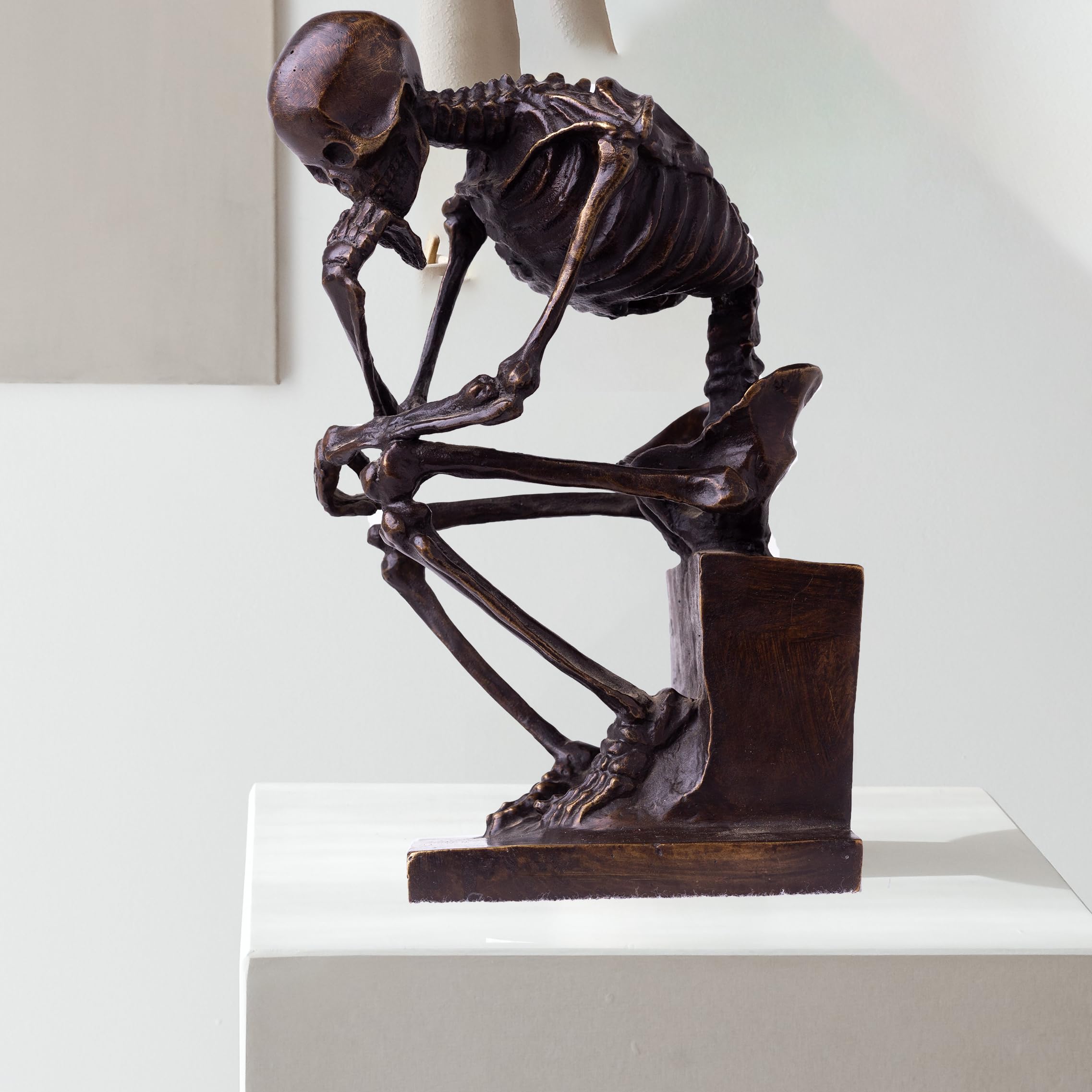 Bronze skeleton Thinker statue in brown bronze finish beside decorative tree ornament