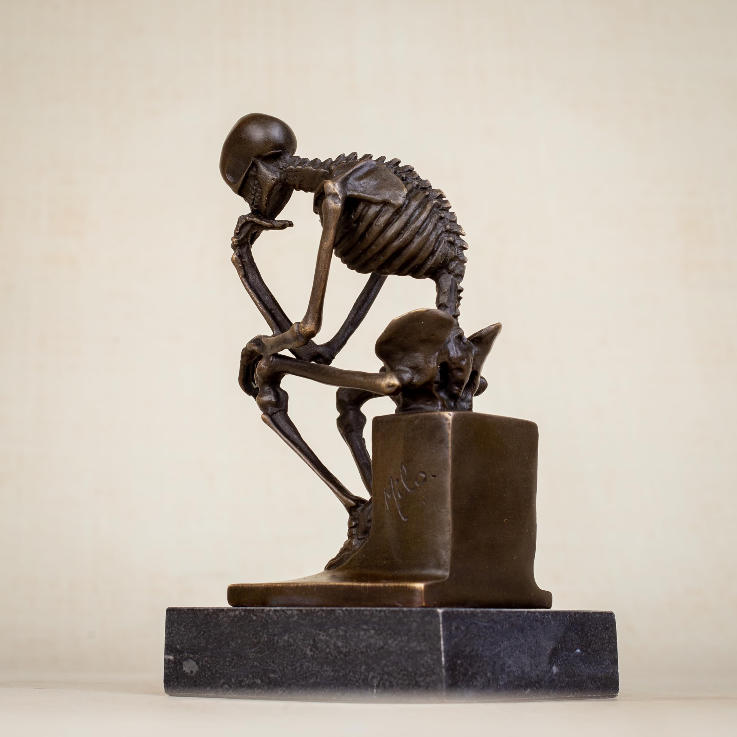 Bronze skeleton Thinker statue in brown bronze finish front view on beige background