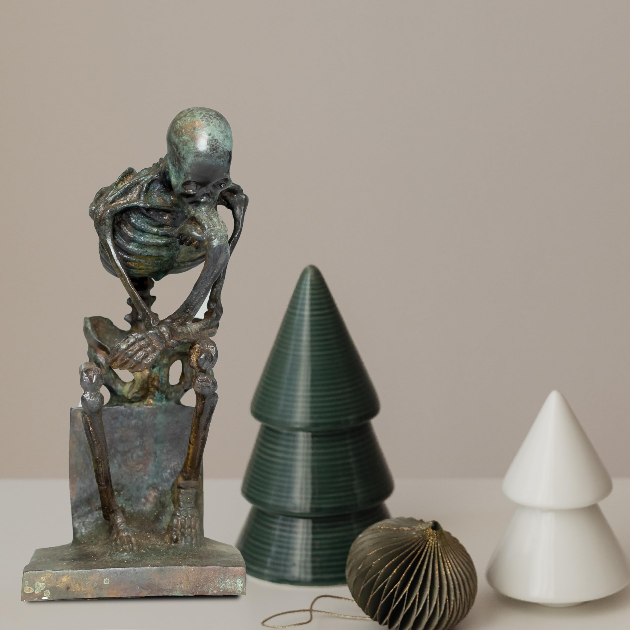 Bronze skeleton Thinker statue in brown bronze finish beside decorative tree ornaments