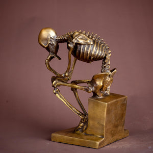 Close-up of bronze skeleton Thinker statue in gold finish on warm brown background