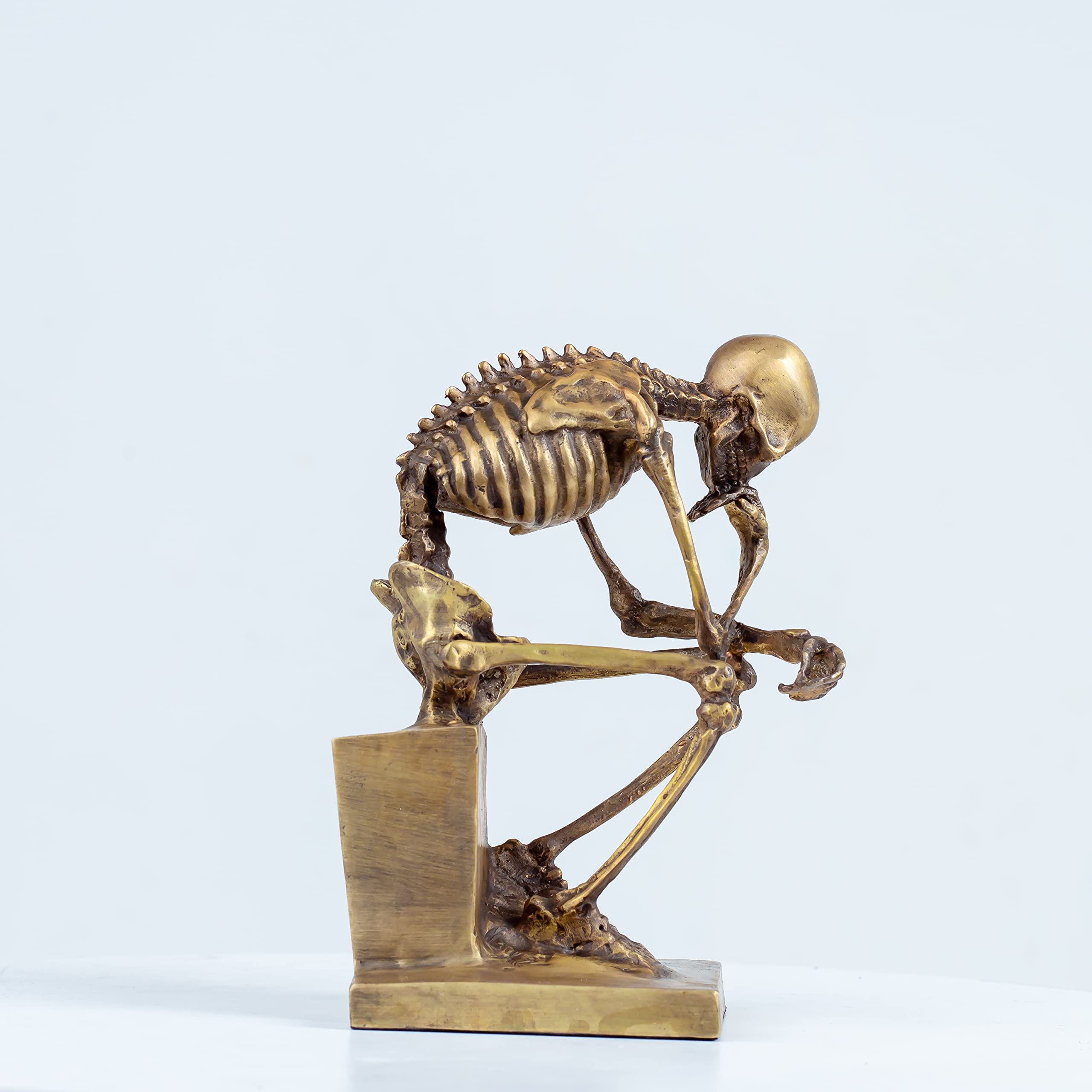 Bronze skeleton Thinker statue in gold finish front view on light blue background