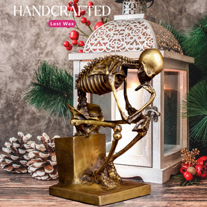 Bronze skeleton Thinker statue in gold finish handcrafted feature beside pinecone holiday decor