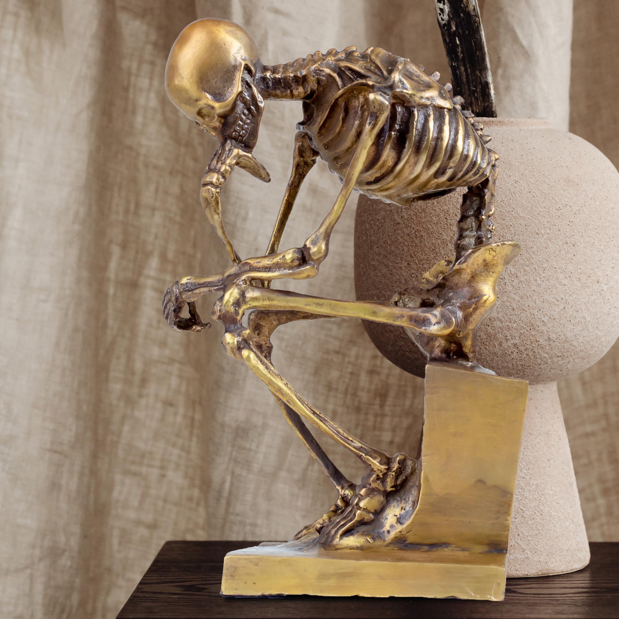 Bronze skeleton Thinker statue in gold finish beside plant and curtain in home decor setting