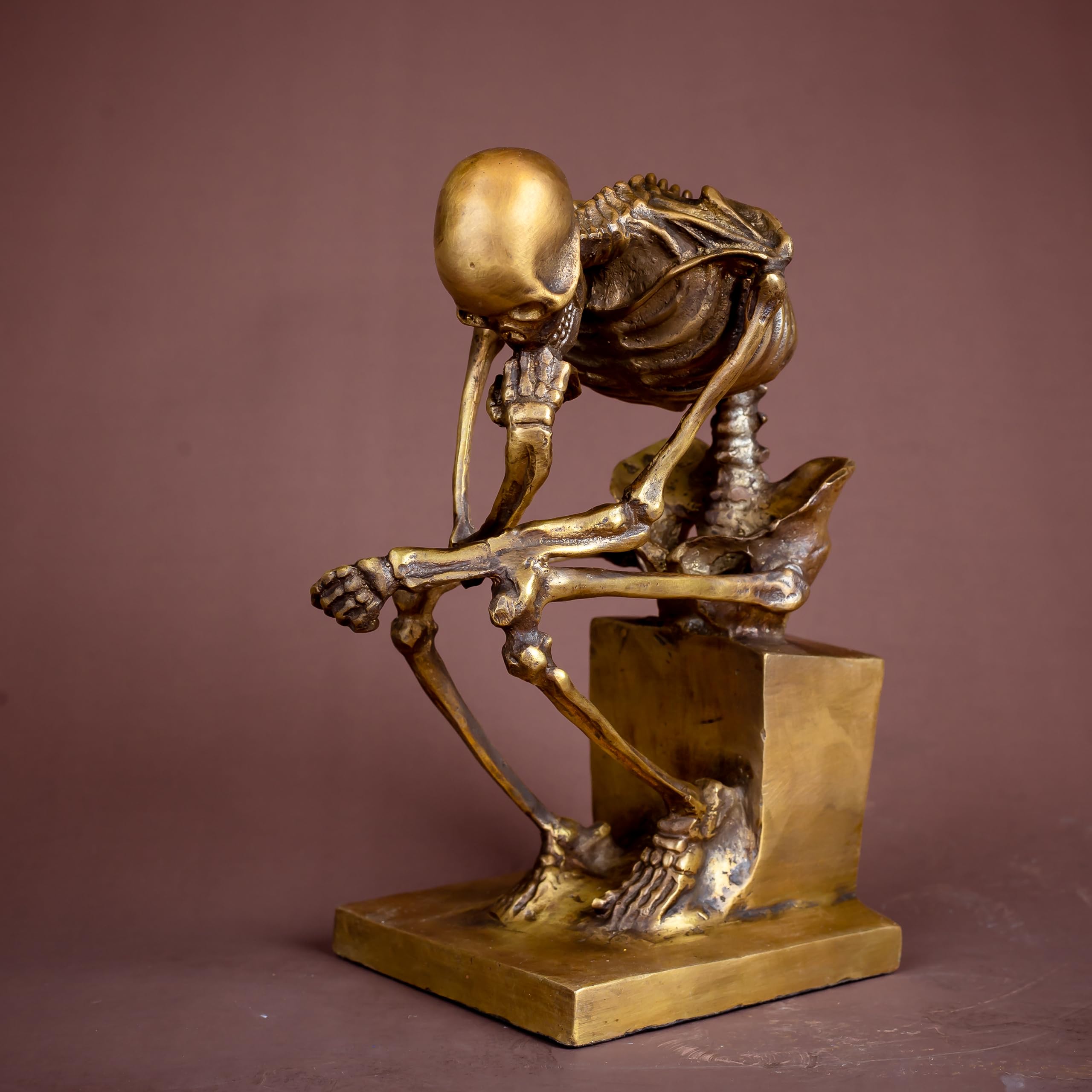 Bronze skeleton Thinker statue in gold finish three-quarter angle view on warm brown background