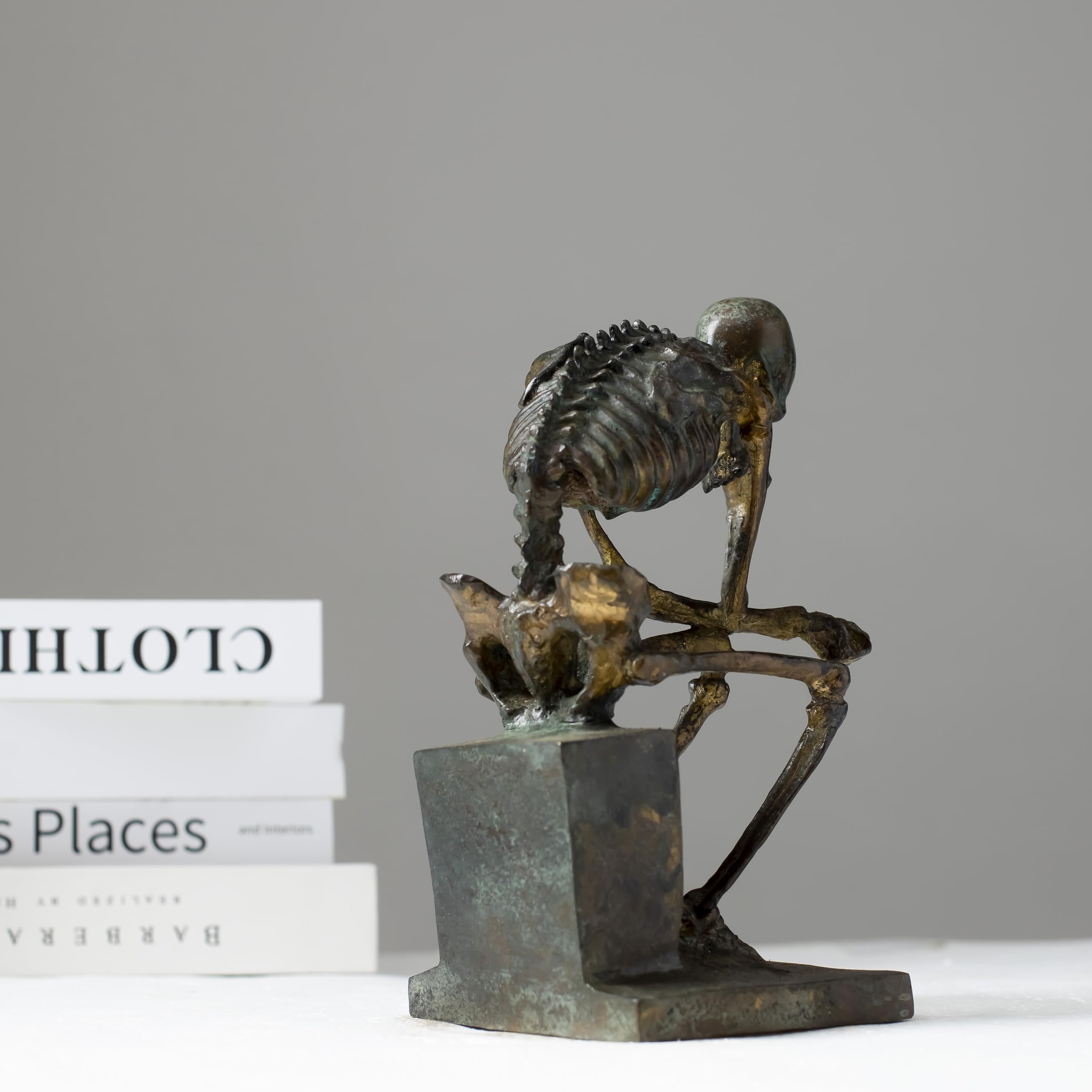 Bronze skeleton Thinker statue in green patina finish displayed on desk beside laptop