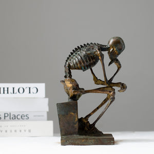 Bronze skeleton Thinker statue in antique grey finish front view beside stacked books