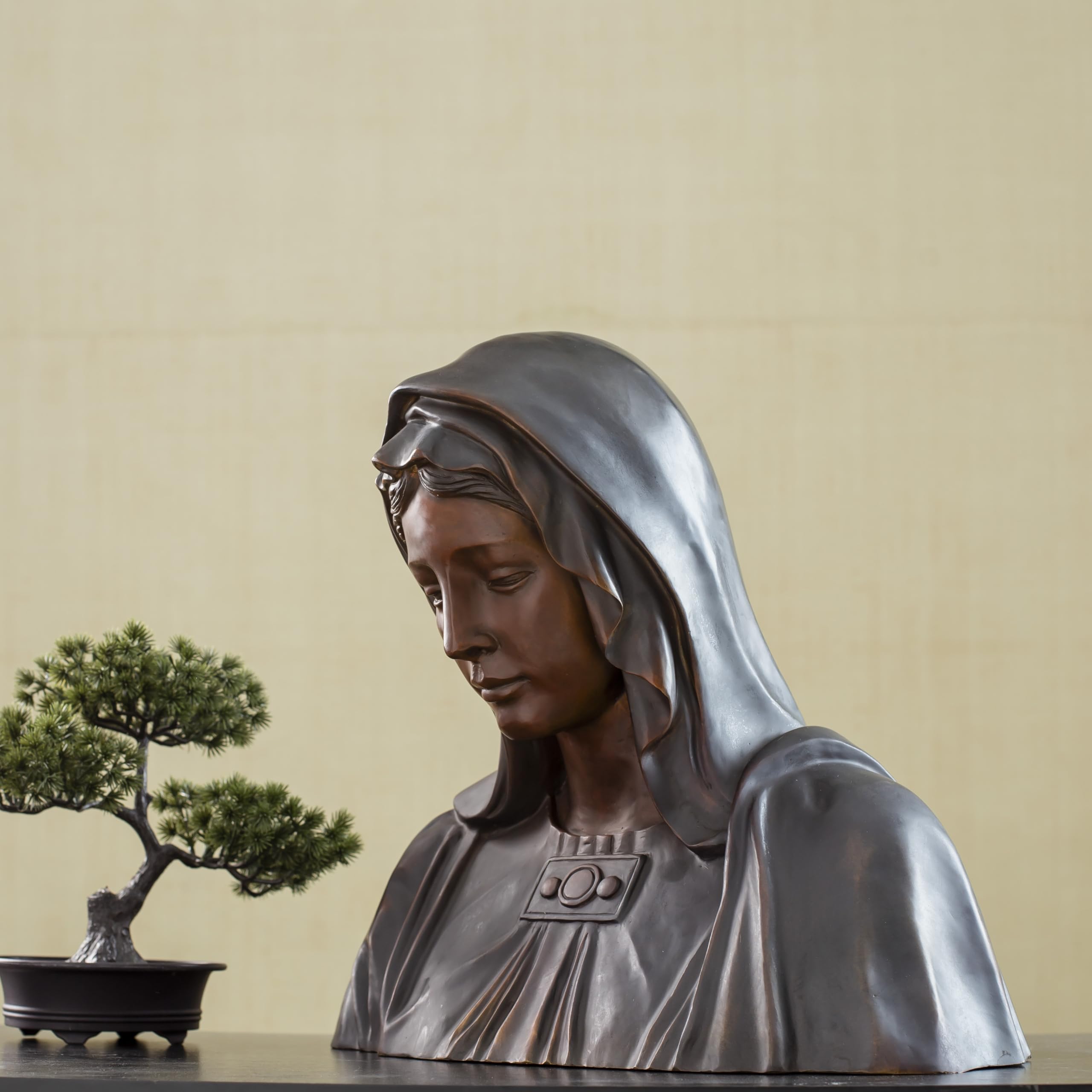 Bronze Virgin Mary bust statue displayed with bonsai tree, front angle view in indoor setting