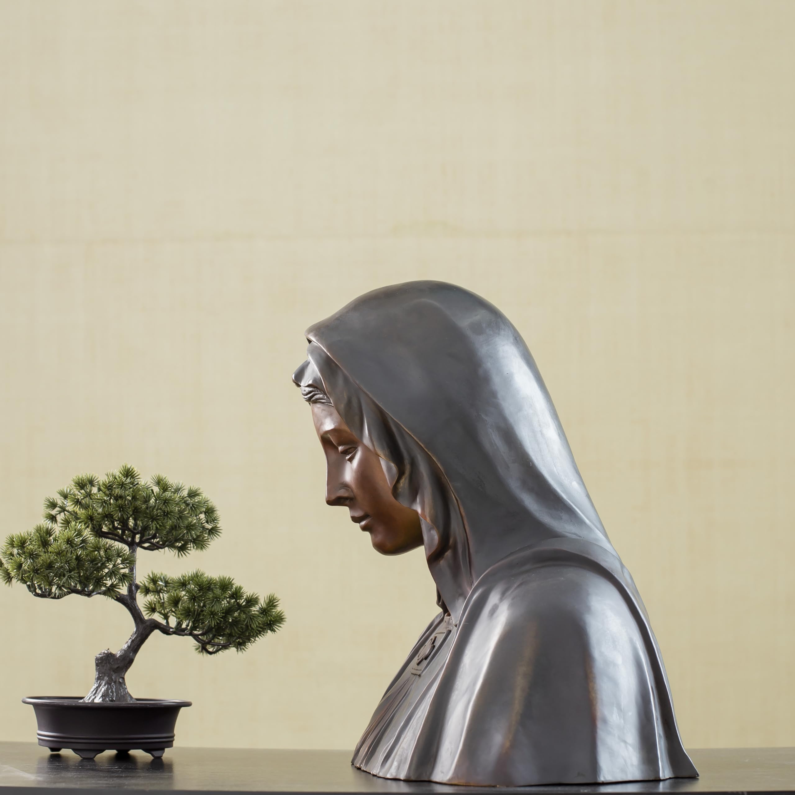 Bronze Virgin Mary bust statue side view displayed alongside bonsai tree in lifestyle setting