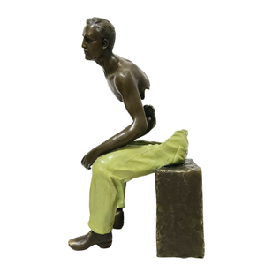 Front view of Les Voyageurs seated bronze fragmented figure with green trousers on cube base
