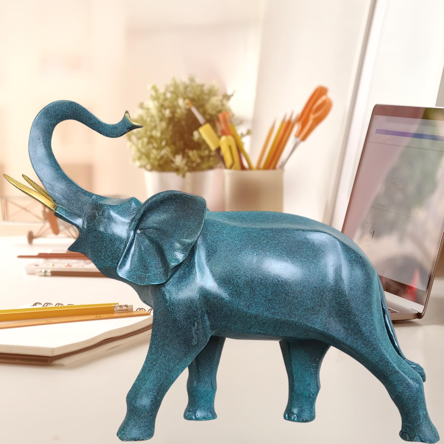 Cerulean blue bronze elephant statue with trunk up on desk beside office supplies and decor items