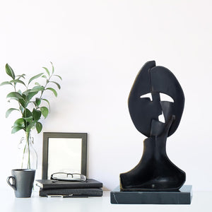 Two cubist mask bronze sculptures displayed on desk with photo frame as contemporary home decor