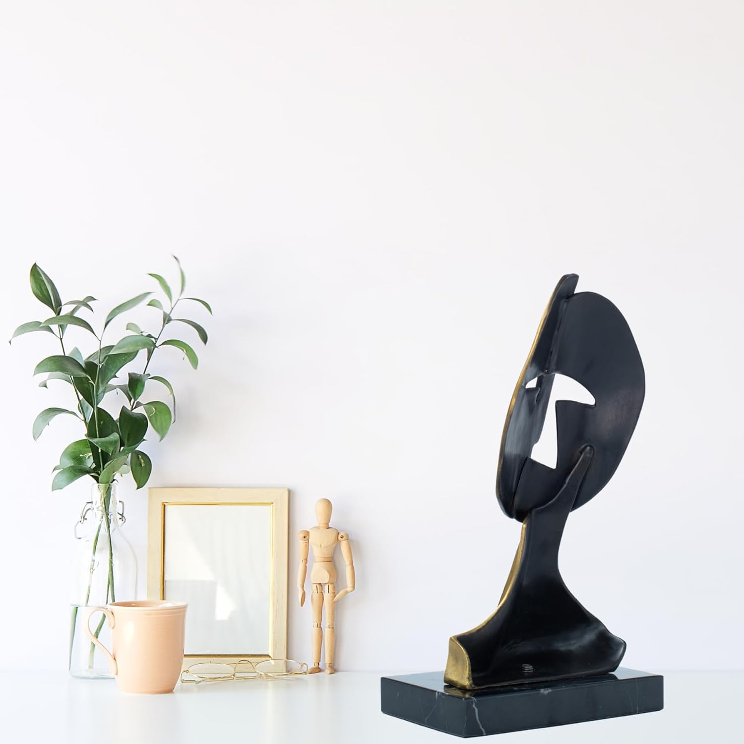 Pair of cubist mask bronze sculptures displayed together with indoor plant in lifestyle setting
