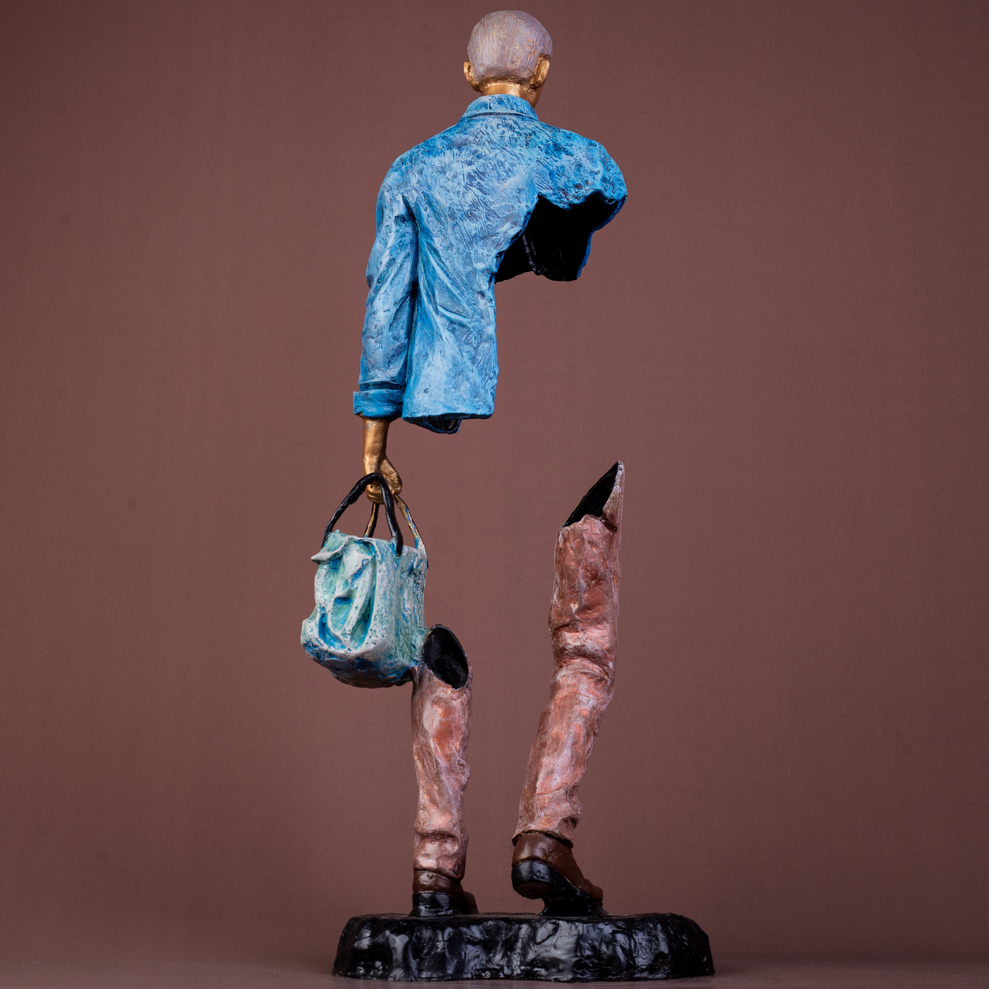 Modern bronze sculpture of a man with fragmented limbs, blue jacket, holding a bag