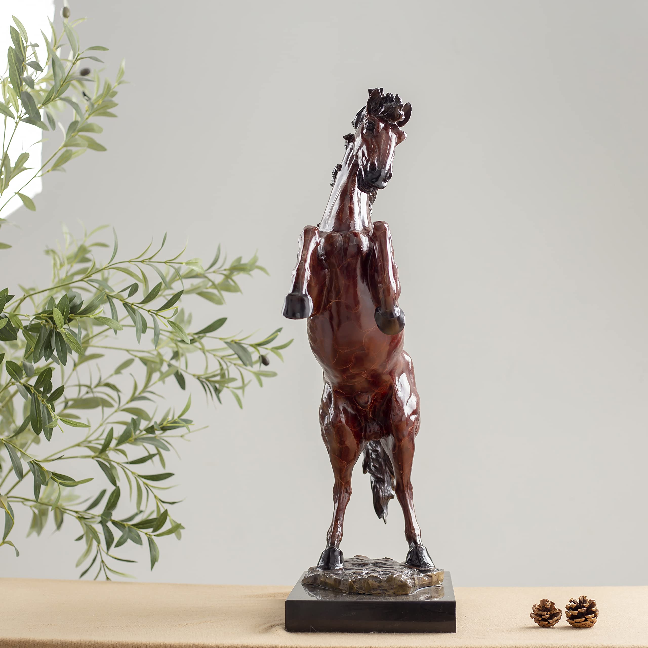 Red bronze rearing stallion sculpture back angle view displayed with greenery decor