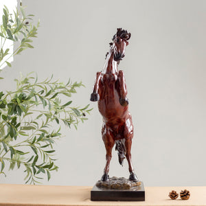 Red bronze rearing stallion sculpture back angle view displayed with greenery decor