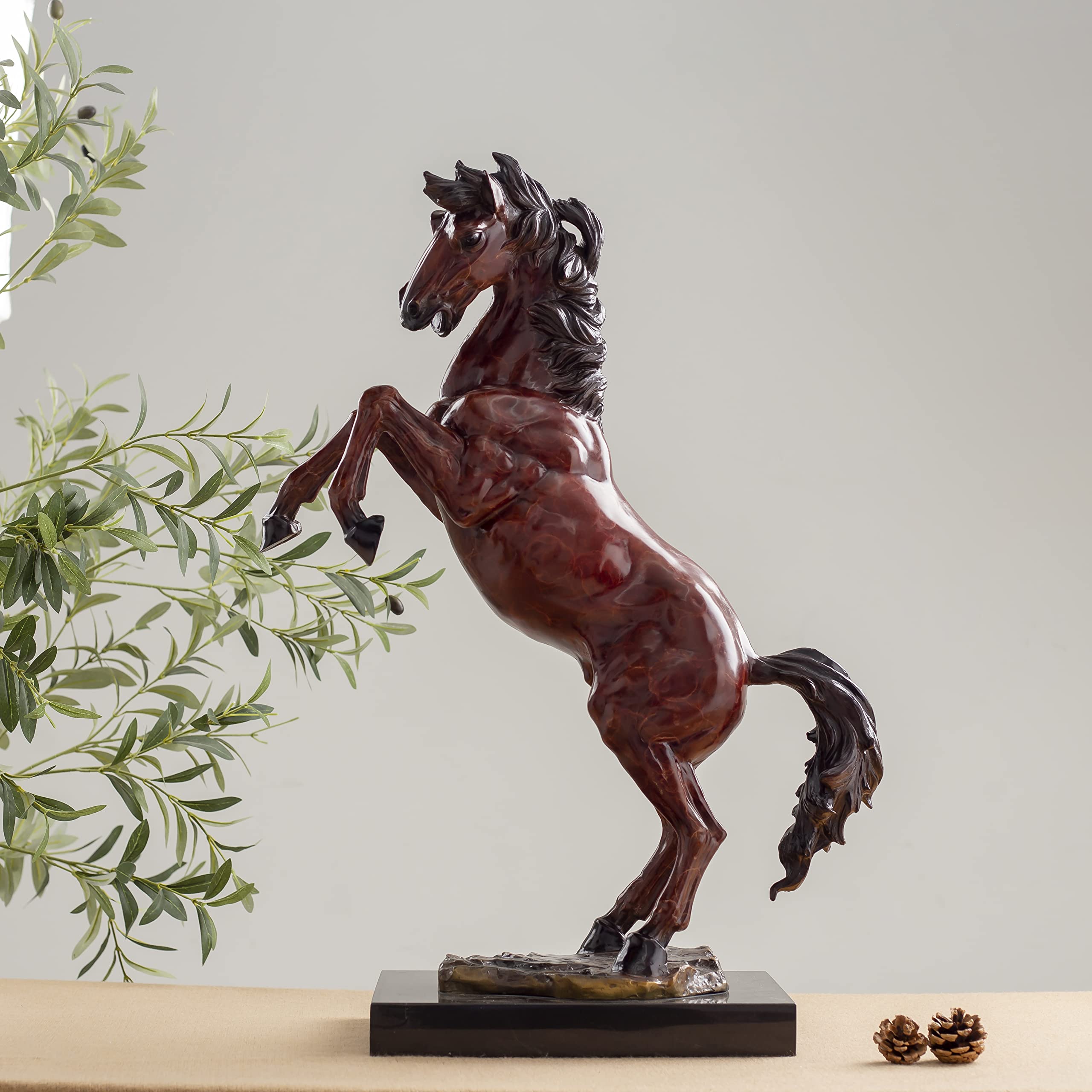 Red bronze rearing stallion sculpture front view displayed with greenery and framed art